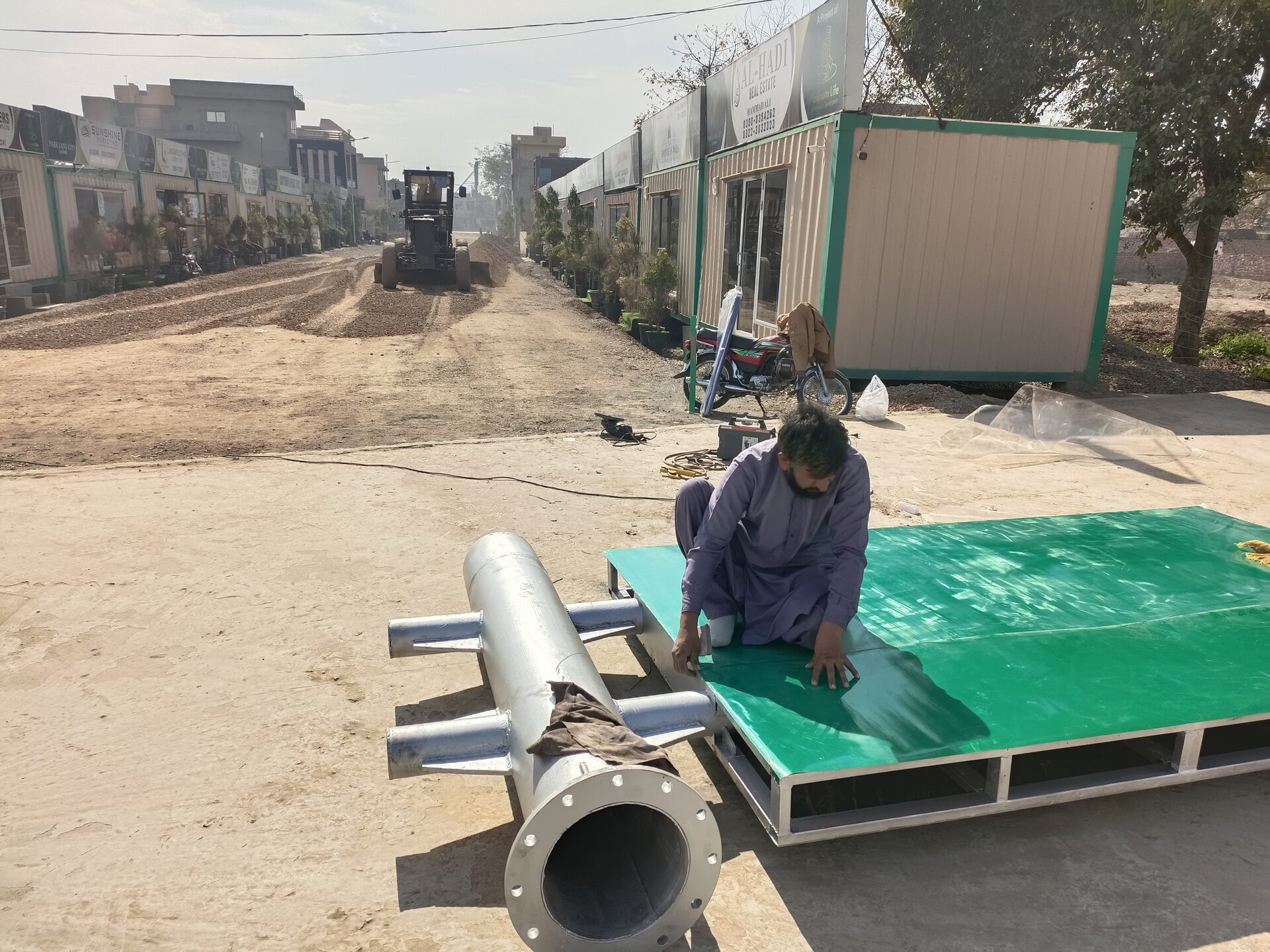 Worker kneeling and installing water pipe system, bulldozer working in background, January 2023